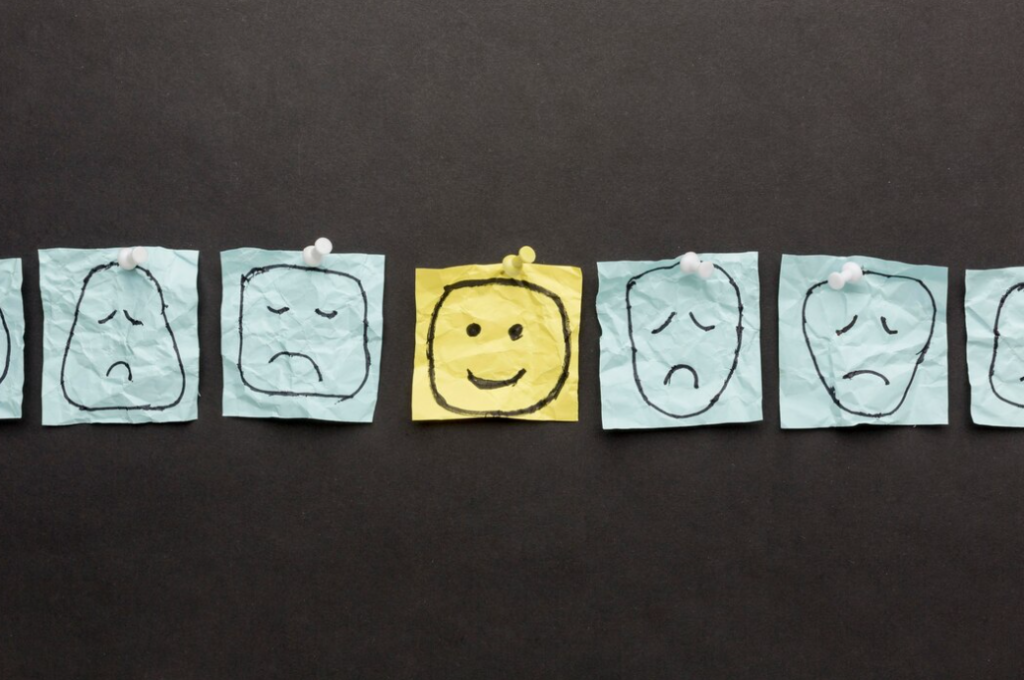 sticky notes on a dark background displaying one smiling face amidst several sad faces