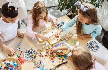 little girls sitting around the table and making decorations for the party