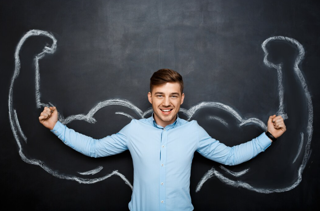 A cheerful man in a light blue shirt poses with chalk-drawn flexed biceps behind him